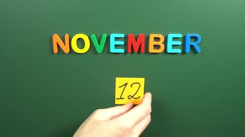 Hand sticking a sticker 12 November calendar day on school board. 12 date of November. Twelfth day