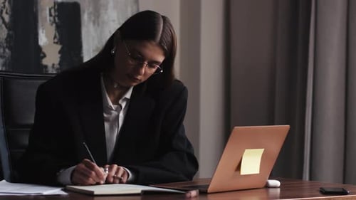 Woman Writes in Notebook at Office Desk