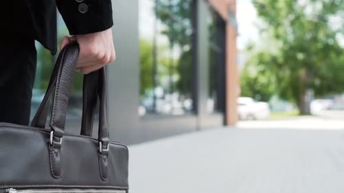 Ambitious businessman walks outdoors holding documents case in the city slow motion
