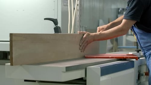 Carpenter works with wooden planks at woodworking factory