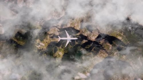 Aerial View of Airplane Flying High Above Rugged Mountain Terrain and Clouds
