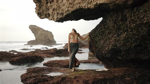 Mujer tocando la roca bajo un arco natural en la playa