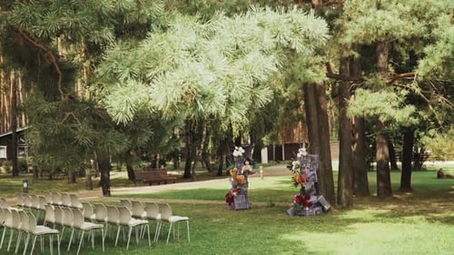 View of Wedding Floral Decorated Arch and White Chairs Under the Pine Tree Slow Motion Outside