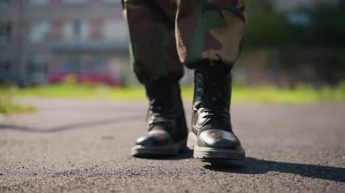 Military Boots Stepping On Asphalt With Close View Of Sole And Laces Camouflage Trousers And Scuffed