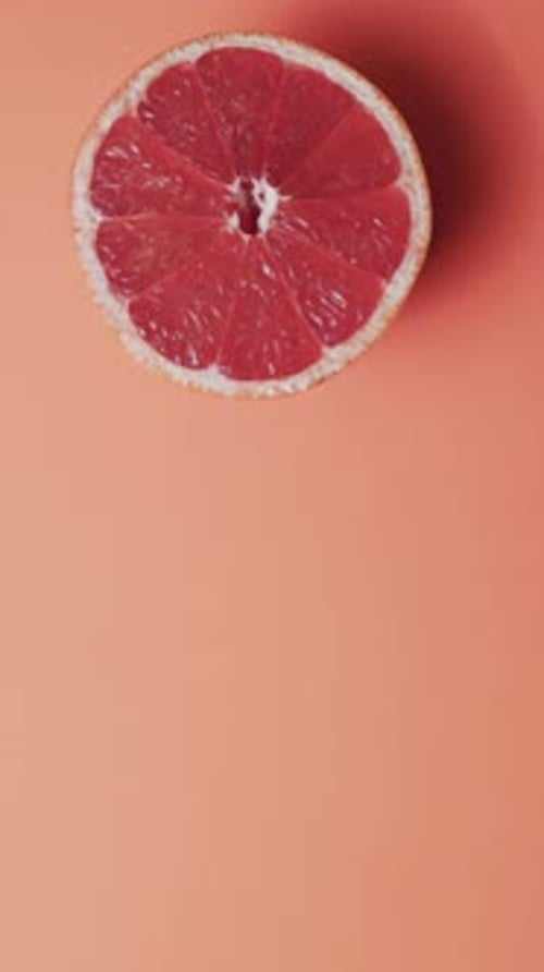 Vertical video of halved red grapefruit with copy space over red background