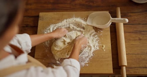 Top View Over Shoulder of Confident Girl Baker Kneading Dough with Flour on Cutting Board in Bakery