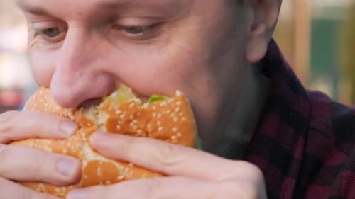 Caucasian man bites an appetizing burger in fast food restaurant. Male eats fast food