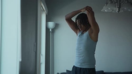 Man Stretching Arms Above Head in Bright Room