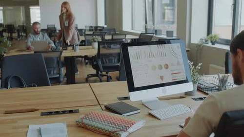 Man Working with Business Graphs on PC and Writing in Copybook in Office