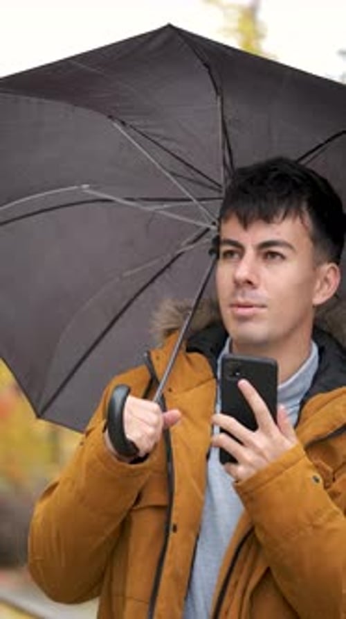 Young Adult Using Phone with Umbrella in Autumn