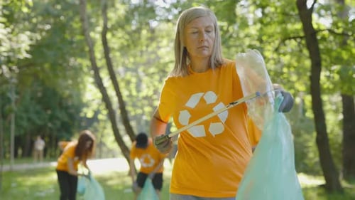 Una mujer caucásica mayor, voluntaria ecológica, usa un recolector de basura mientras recolecta plástico en un grupo de bolsas de basura
