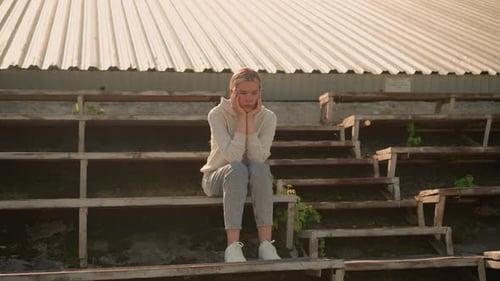Pensive Woman in Hoodie Sitting on Rustic Stadium Bleachers