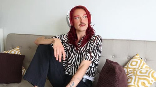 Young non-binary person listening to music with headphones on sofa