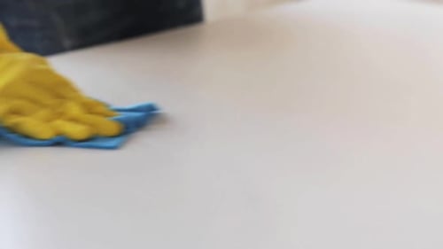 Gloved hand cleaning white table surface with rag