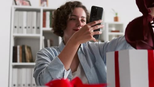 Woman Photographing Gifts with Mobile Phone at Home