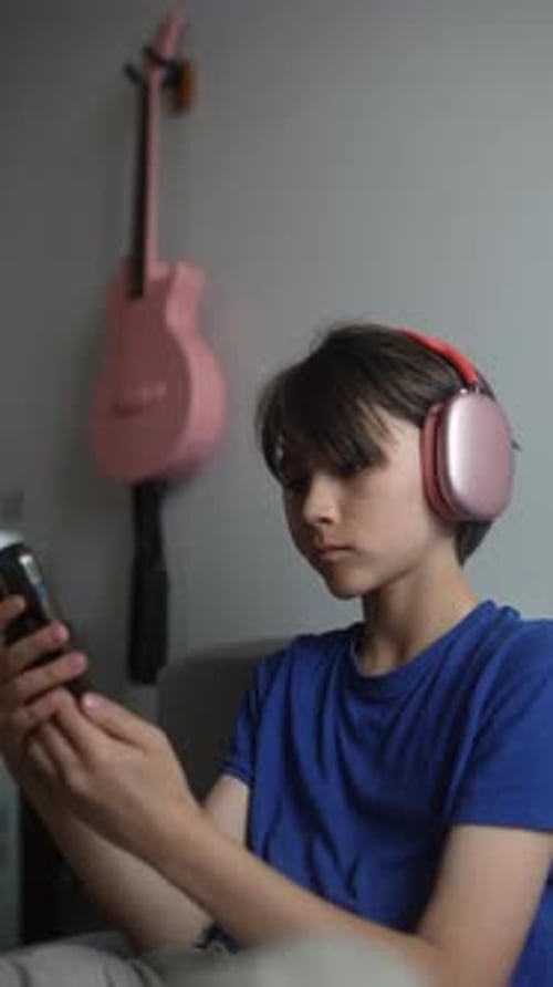 A Young Boy Enjoys Music Through Headphones While Using His Smartphone Creating a Chill Vibe