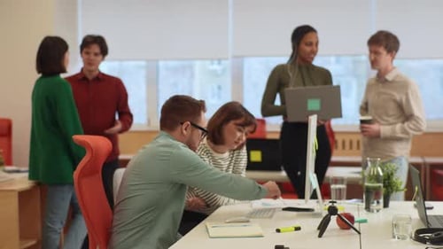 Seitenansicht eines männlichen Mentors und einer Praktikantin, die mit Laptop am Schreibtisch sitzen und gemeinsam Papierkram erledigen
