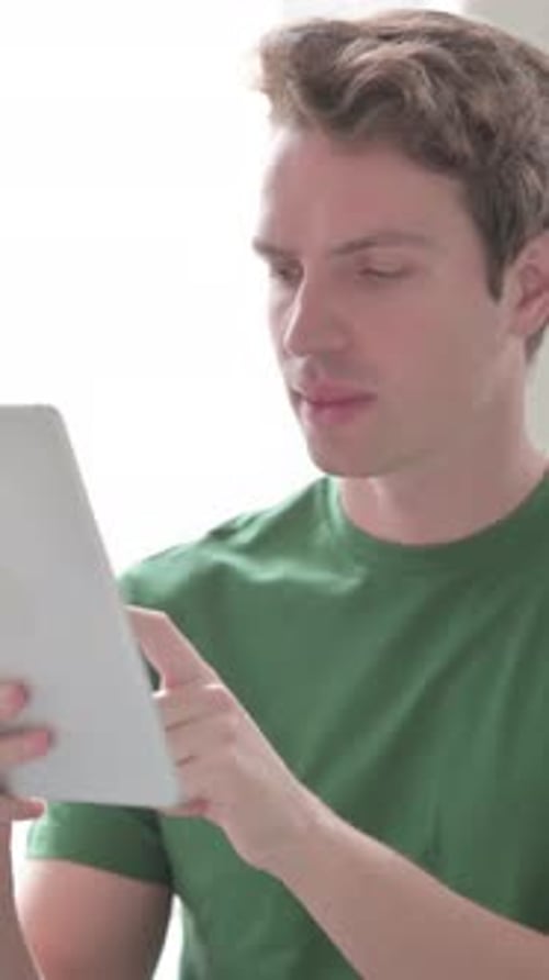 Young Man Using Tablet Device Indoors, Reacting with Frustration