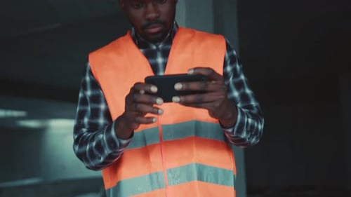 Professional AfroAmerican Engineer Works on Blueprint and Meanwhile Uses Smartphone Then Makes a