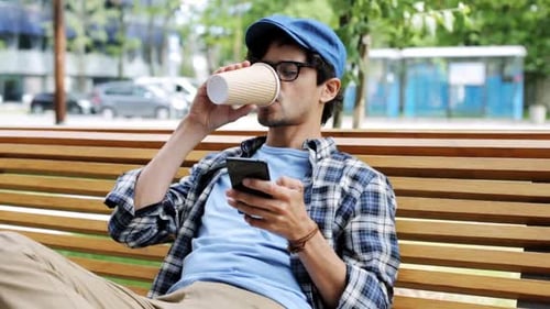 Man Uses Phone and Drinks Coffee on Bench