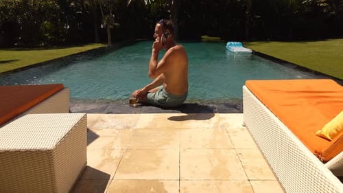 Man relaxing by pool talking on cellphone