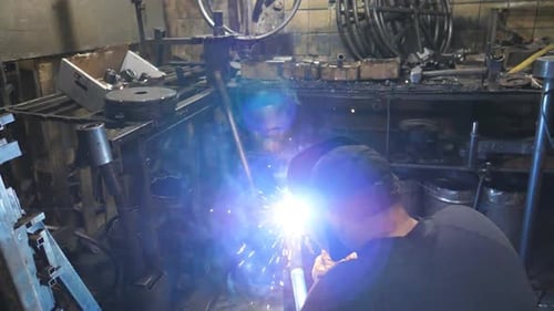 Arbeiter beim Schweißen von Metallkonstruktionen mit Schutzmasken bei Schweißarbeiten in der industriellen Produktion