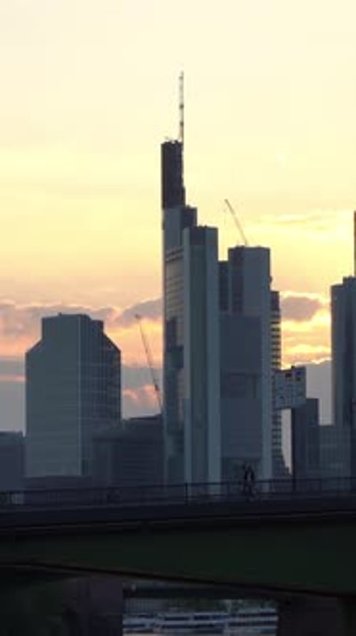 People Walking on Bridge with Modern Skyscrapers and Cranes at Sunset Skyline