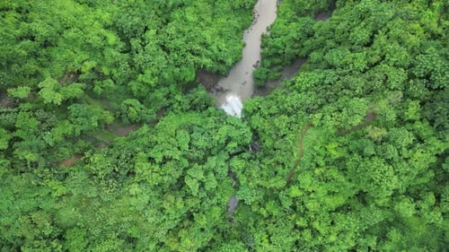 A top view of lush green mountains with a waterfall cascading down into the source of a small river.