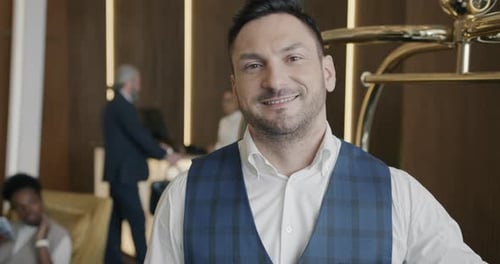 Smiling Bellhop Standing in Hotel Hall Next to Baggage Cart and Looking at Camera