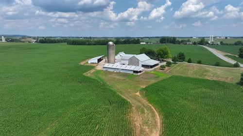 Aerial approaching shot of farm house with barn and silo storage during cloudy day. American country
