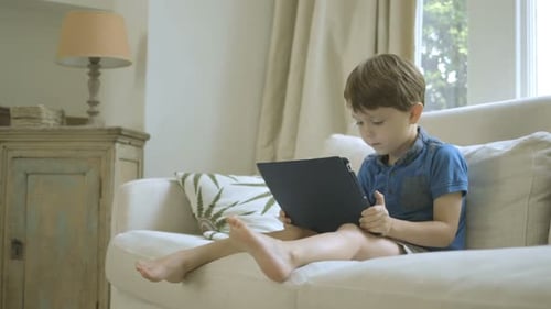Boy plays with tablet on sofa in living room