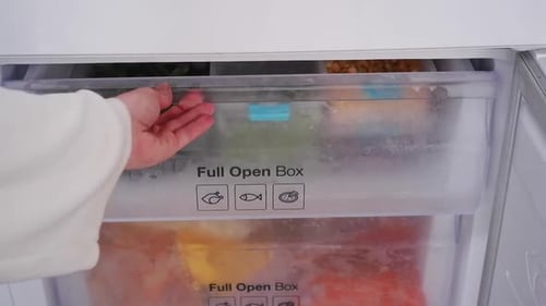 Hand Opens Freezer Drawer with Frozen Vegetables