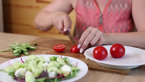 06 1Frau schneidet frische rote Tomaten auf einem Schneidebrett in Scheiben und legt sie auf einen Salatteller mit Gurken,