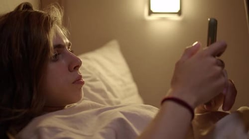 Young Adult Using Mobile Phone in Bed at Night