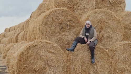 Man Sits on Hay Bales in Rural Field