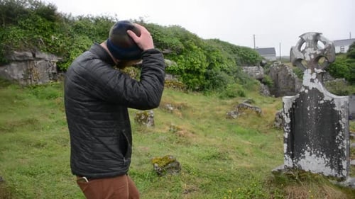 Un homme au cimetière pleure sous la pluie devant une vieille pierre tombale blanche