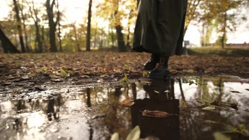 Woman in Boots Walking Past a Puddle in an Autumn Park