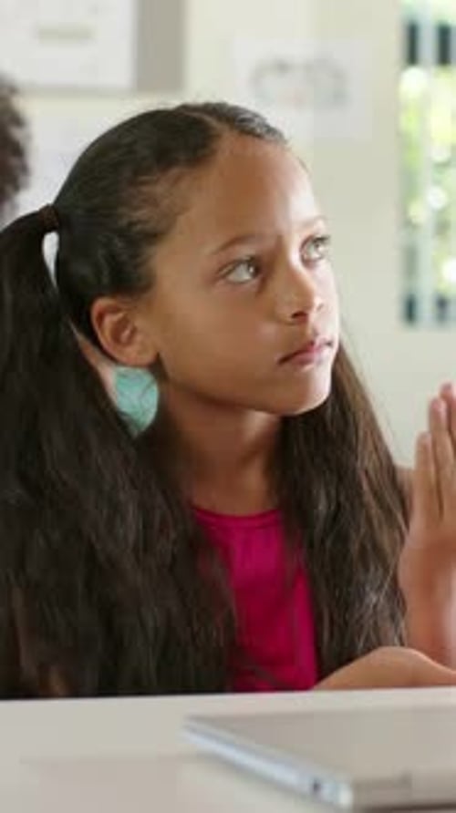 Vertical video: Listening girl in pink top tapping chin at offframe speaker in class, with laptop