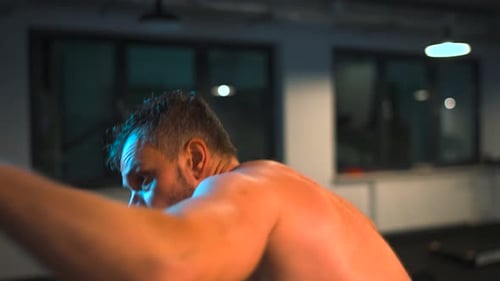 Alone Boxer is Working Out Blows on a Punching Bag in a Gym in Evening