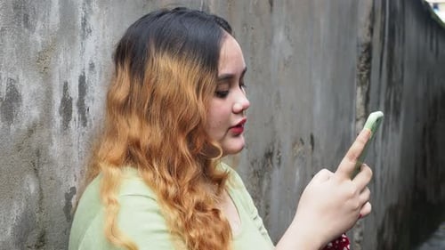 Young Woman Uses Smartphone Outside by Wall