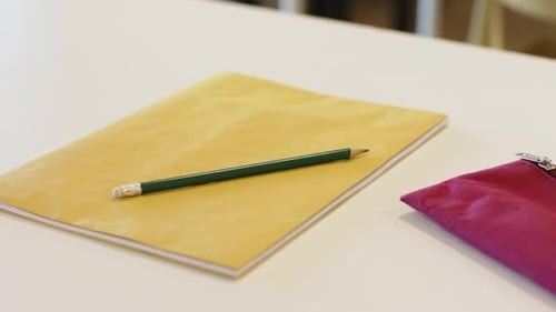 Camera is zooming and focusing, keeping yellow notebook with green pencil still on desk for display