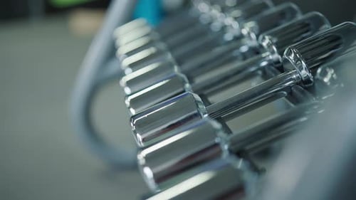 Shiny metallic dumbbell rack at indoor gym facility with blurry background