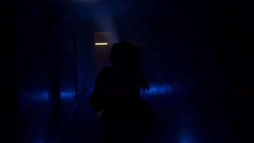 Woman with a Flashlight Runs Along a Dark Corridor