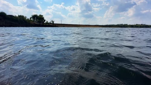 Uneven surface of river. Little waves move in the wind. Close up. Waterfront and sky at backdrop.