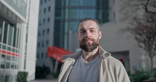 A Young Man with a Stylish Trendy Hairstyle and Beard in Casual Clothes Stands on the Street in the