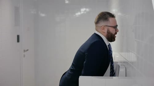 Man in Suit Using Urinal in Public Restroom