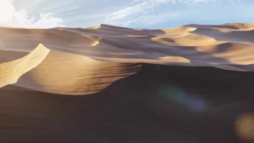 Travelling Across the Sand Dunes of a Desert Landscape as the Sun Sets over a Blue Sky