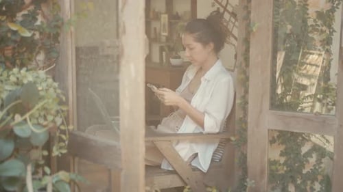 Woman Using Phone in Sunlit Wooden Patio