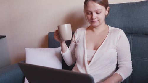 Woman Uses Laptop and Drinks Coffee at Home