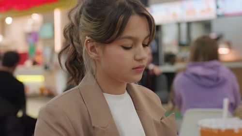 Young White Woman at Mall Table Tasting Chip with Curious Expression Colorful Foodcourt Lights and